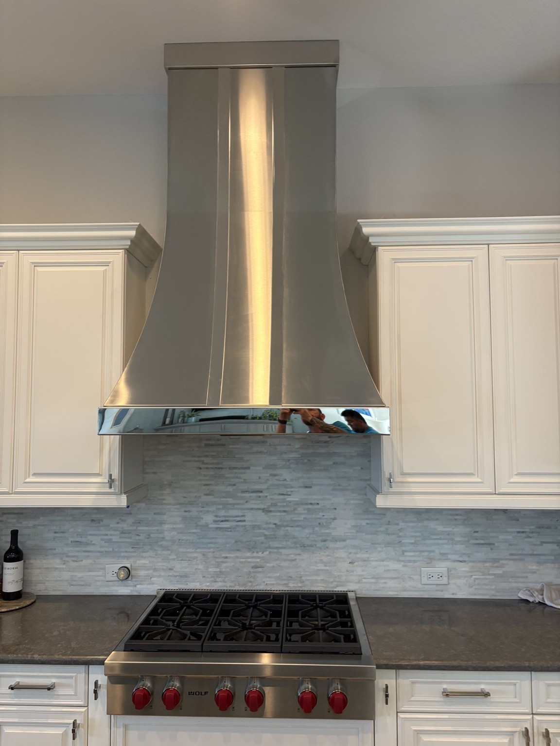 Custom stainless hood above a Wolf rangetop, fitted between white cabinets